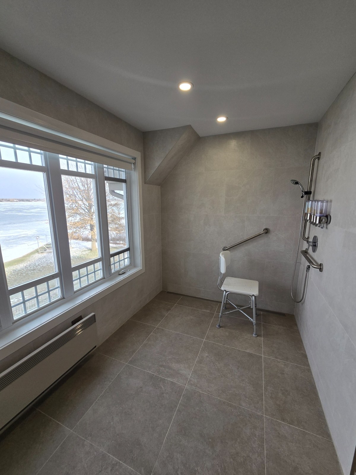 Vue large de la douche en céramique avec grande fenêtre, barres d’appui et éclairage encastré